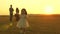 Happy child and parents walk at sunset. Dad hugs daughter and whirls in flight. Silhouette of a family walking in the