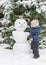 Happy child playing with a snowman outdoor in winter. Cute little child building a snowman and having fun in park or backyard