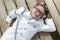 Happy child resting on a wooden plank dressed in communion suit. Lying down on wooden table wearing a white sailor suit