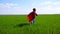 A happy child in a superhero costume in a red cape and in a mask runs on green grass on a sunny day