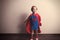 Happy child in superhero suit against gray wall.