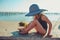 Happy child in swimsuit and hat relaxing on the summer beach and getting some tan.