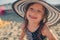 Happy child in swimsuit and hat relaxing on the summer beach and getting some tan.