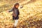 Happy child walking in autumn park. Baby girl throwing the fallen leaves up. Beautiful golden autumn time. Happy and healthy child