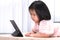 Happy child watching cartoon on tablet at living room in her house. Kid lying down on the wood table. Sweet girl wearing soft pink