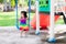 Happy child wearing a bright rainbow dress  sitting on a swing. Children play in the playground. Asian girl look sideways.