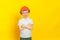 Happy child worker stands in a hard hat on a yellow background.