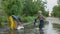 Happy childhood, attractive male kids in overalls pours out rubber boot after having fun playing in puddle by road after