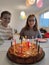 Happy children at birthday party with torte and colorful candles at table at home