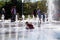 Happy children laugh and splash in fountain in the summer park. People walk in the summer park