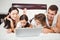 Happy children with parents using laptop on bed