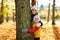 Happy children peeking out tree at autumn park