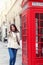 Happy city traveler woman stands next to a red telephone booth n London