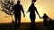 Happy, close-knit family with children, silhouette of farmers outdoors holding hands at sunset. Dad holds a young tree