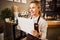 Happy coffeehouse waiter in aprons holding white paper in hand