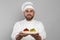 Happy confectioner in uniform holding plate with delicious tartlets on light grey background