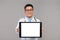 Happy confident adult japanese doctor in white coat and glasses shows tablet with blank screen