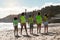 Happy confident diverse teen kids volunteers in vests raise hand up, celebrating victory over trash on beach