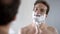 Happy and confident male putting shaving cream on his face before shaving