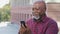 Happy contented senior black grandfather man making video call, looking at smartphone camera, showing thumb up approval