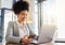 Happy corporate employee texting on a phone while working on a laptop in an office, reading email. Young professional