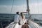 A happy couple dressed in white are standing on the deck of a luxurious yacht that& x27;s sailing on the ocean