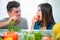 Happy couple eating fruit and vegetables for morning breakfast - Young people preparing healthy meal at home during quarantine