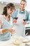 happy couple in flour with wineglasses cheering at kitchen beside bowl with dough