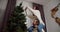 Happy couple guy and girl decorate the New Year tree, the guy helps his girlfriend who sits on his shoulders and