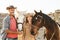 Happy couple having fun with horses inside stable - Young farmers sharing time with animals in corral ranch