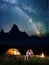 Happy couple hikers covered with a plaid sitting together under starry sky near campfire and camp at night