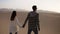 Happy couple holding hands walking in romantic relationship under sun and blue sky in desert. Two young lovers walking