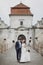 Happy couple of newlyweds walking near castle, fairytale wedding moment beautiful bride and groom hug near ancient castle entrance