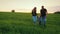 A happy couple of parents with a small son are walking across the field towards the sunset. Happy family with a child