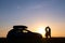 Happy couple relaxing beside their SUV car during honeymoon road trip at sunset. Young man and woman enjoying time together