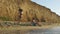 Happy couple on sandy beach with high sandstone cliffs. Young playful girl playfully runs around handsome sitting man