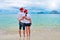 Happy couple in Santa hats relaxing on tropical sandy beach near sea, Christmas and New Year holiday vacation