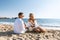 Happy couple seating with champagne on the beach. Summer vacations concept