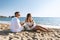 Happy couple seating with champagne on the beach. Summer vacations concept