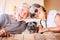 Happy couple of senior caucasian people have fun and smile with funny nice old dog pug in the middle sitting on the table together