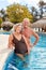 Happy couple of seniors is standing in swimming pool in summer vacation