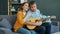 Happy couple singing playing the guitar in apartment enjoying leisure time together