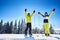 Happy couple skiers standing on mountain edge, rejoicing, raising hands up. Clear blue sky over winter mountain nature.