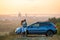 Happy couple spending time together near their SUV car during honeymoon road trip at warm summer evening. Young man and woman