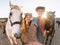 Happy couple taking selfie with horses inside stable - Young farmers having fun with animals in corral ranch