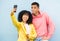 Happy couple, tongue and phone selfie on isolated blue background for social media, city profile picture and travel vlog