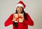Happy crazy excited young woman in santa claus hat with christmas present laughing and smiling