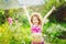 Happy curly girl under water splashes in the summer garden.