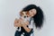 Happy curly woman tilts head, holds pedigree dog, has cheerful expression, smiles pleasantly, has curly hairstyle, wears white t