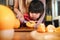 Happy Cute 3-4 Years Old Girl with her Mom Slice some Orange on Wooden Table in Pantry Room. Young Girl is Learning Cook with her